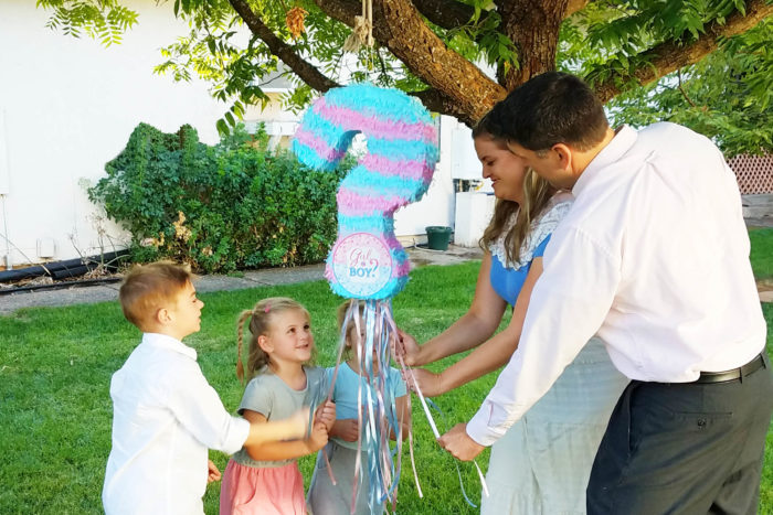 A family pulls on strings of a blue and pink question mark pinata.